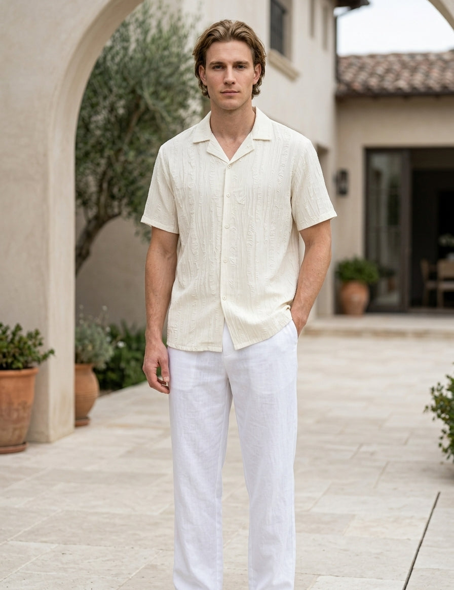 Man wearing a light-colored shirt and white pants standing outdoors.