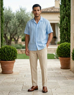 Man wearing a light blue shirt and beige pants standing outdoors near potted plants.
