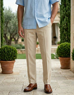 Man wearing a light blue shirt and beige pants standing outdoors with potted plants and a stone pathway.
