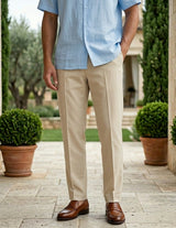 Man wearing a light blue shirt and beige pants standing outdoors with potted plants and a stone pathway.