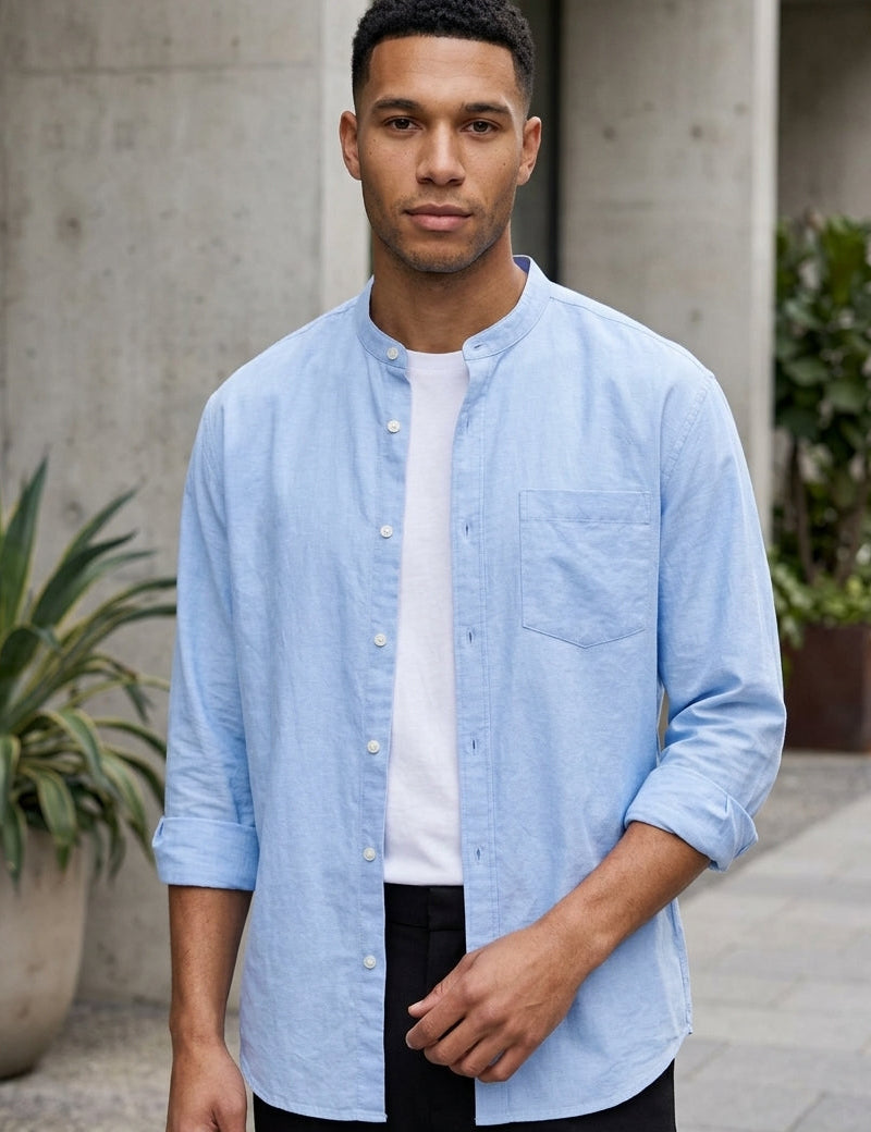 Man wearing a light blue shirt over a white t-shirt with black pants, standing outdoors.