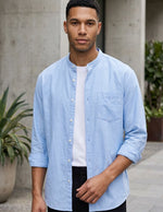 Man wearing a light blue shirt over a white t-shirt with black pants, standing outdoors.