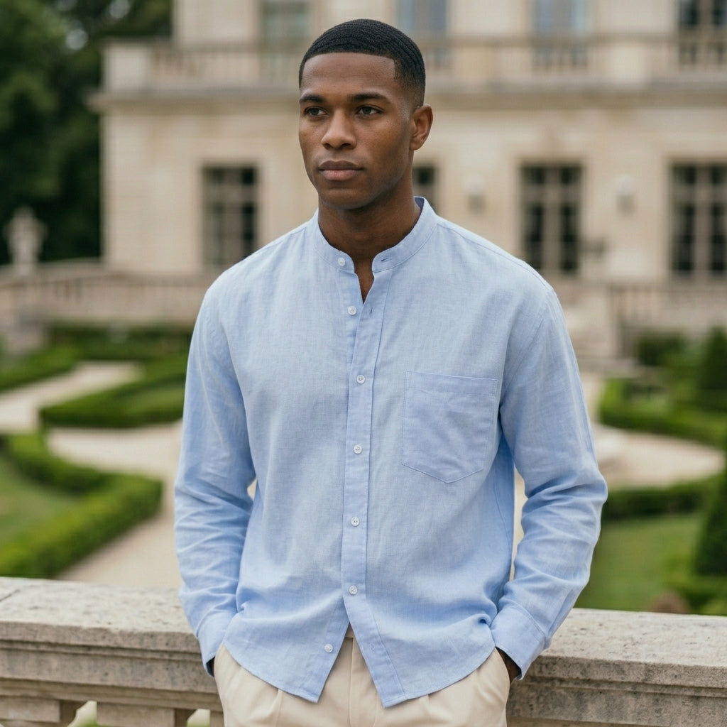 Man wearing a light blue shirt standing in front of a classical building with greenery.