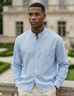 Man wearing a light blue shirt standing in front of a classical building with greenery.