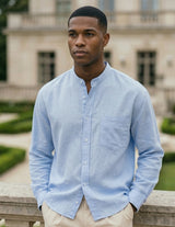 Man wearing a light blue shirt standing in front of a classical building with greenery.