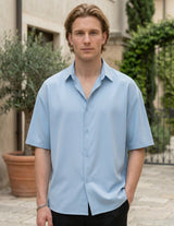 Man wearing a light blue shirt standing outdoors with plants in the background
