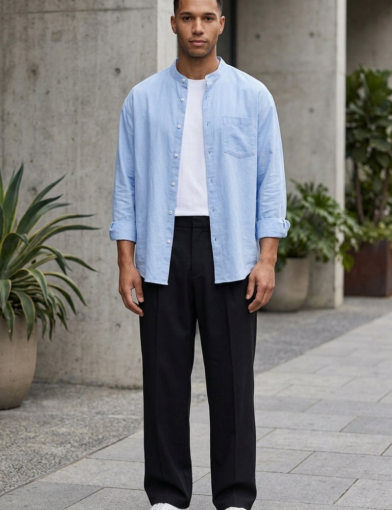 Man wearing a light blue shirt, white t-shirt, black pants, and white sneakers on a street.