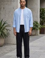 Man wearing a light blue shirt, white t-shirt, black pants, and white sneakers on a street.