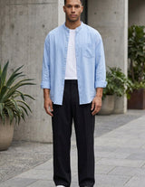 Man wearing a light blue shirt, white t-shirt, black pants, and white sneakers on a street.