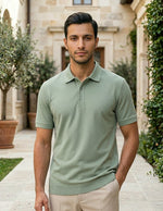 Man wearing a light green polo shirt standing outdoors with a building and trees in the background