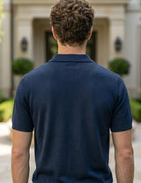 Man wearing a navy blue polo shirt standing in front of a building with greenery.