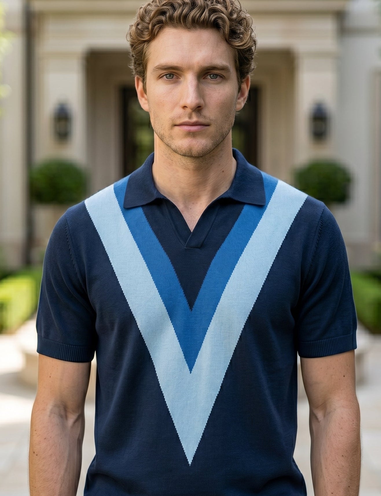 Man wearing a navy blue polo shirt with a large light blue 'V' pattern standing in front of a building.