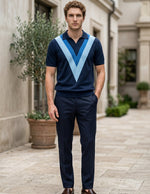 Man wearing a navy blue polo shirt with a light blue V-neck design and dark pants, standing in an outdoor setting.