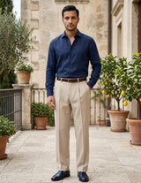 Man wearing a navy shirt and beige pants standing in an outdoor setting with plants and stone walls.