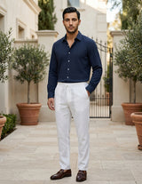 Man wearing a navy shirt and white pants standing in an outdoor setting with potted plants.