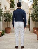 Man wearing a navy shirt and white pants standing in an outdoor setting with potted plants.