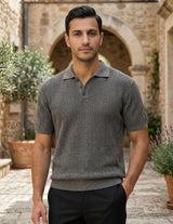 Man wearing a patterned short-sleeve shirt standing in an outdoor setting with stone architecture and plants.