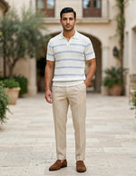 Man wearing a striped polo shirt and beige pants standing in an outdoor setting with plants and buildings.