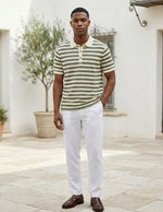 Man wearing a striped polo shirt and white pants standing outdoors.