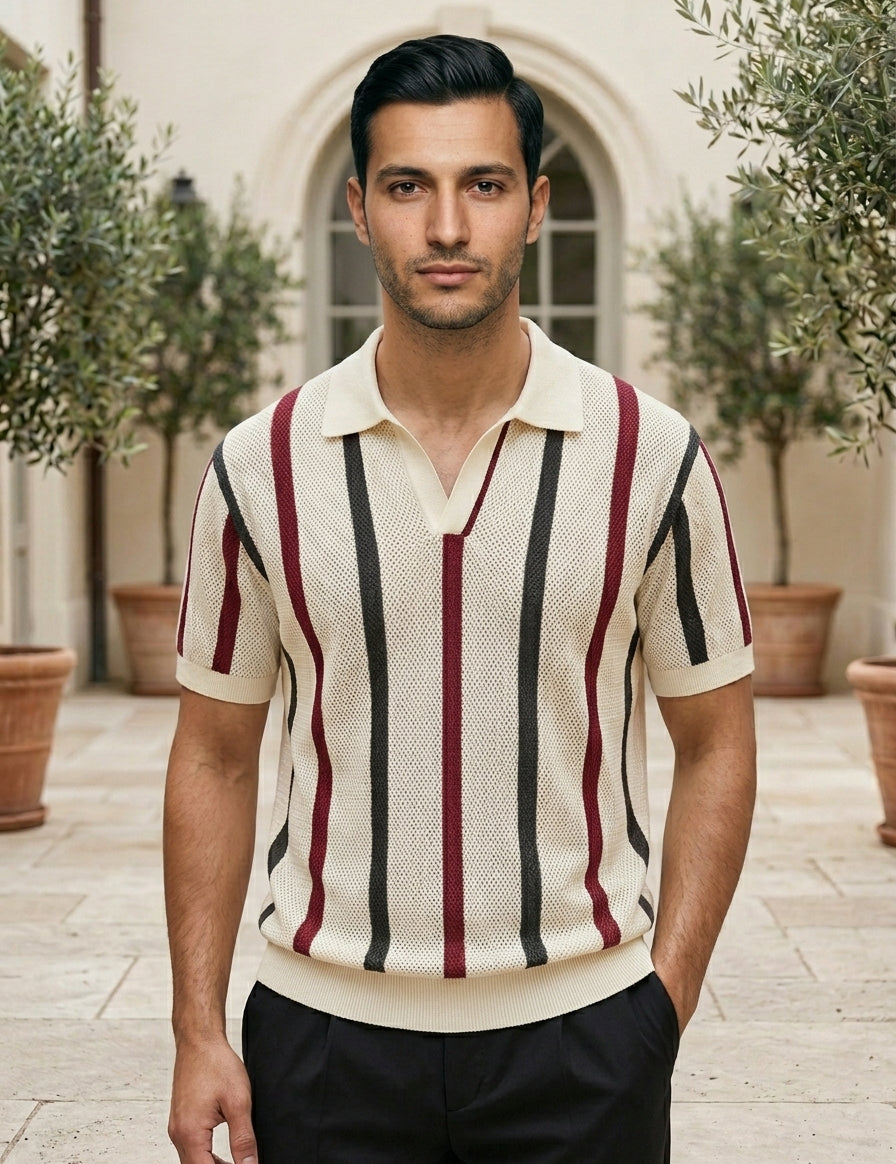 Man wearing a striped polo shirt standing outdoors with plants and a building in the background
