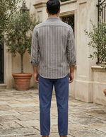 Man wearing a striped shirt and blue pants standing in an outdoor setting with potted plants.