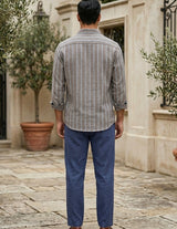 Man wearing a striped shirt and blue pants standing in an outdoor setting with potted plants.