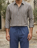 Man wearing a striped shirt and blue pants standing outdoors.
