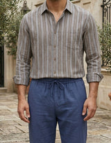 Man wearing a striped shirt and blue pants standing outdoors.