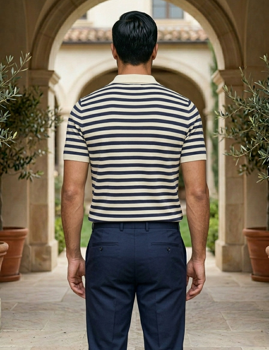Man wearing a striped shirt and dark pants standing in an outdoor setting with arches and plants.
