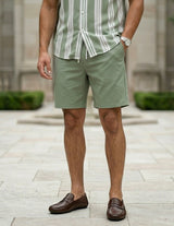 Man wearing a striped shirt and green shorts standing outdoors.