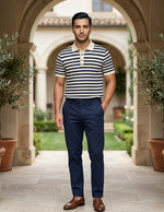 Man wearing a striped shirt and navy pants standing in an outdoor setting with arches and plants.