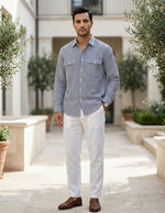 Man wearing a striped shirt and white pants standing in an outdoor setting with plants.