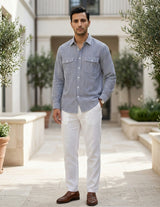 Man wearing a striped shirt and white pants standing in an outdoor setting with plants.