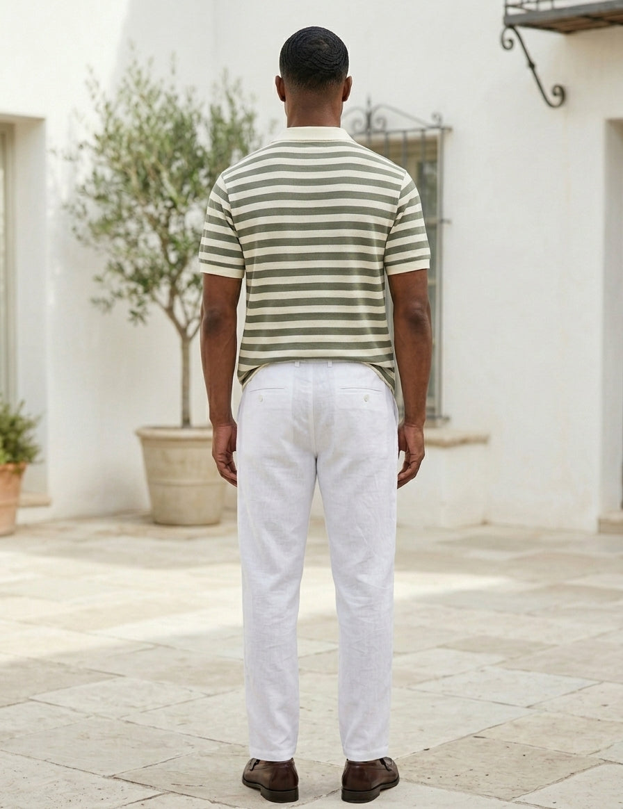 Man wearing a striped shirt and white pants standing in front of a white building.