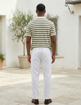 Man wearing a striped shirt and white pants standing in front of a white building.