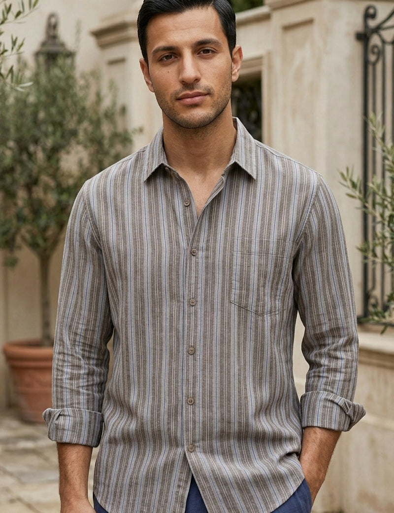 Man wearing a striped shirt standing outdoors with plants and a building in the background
