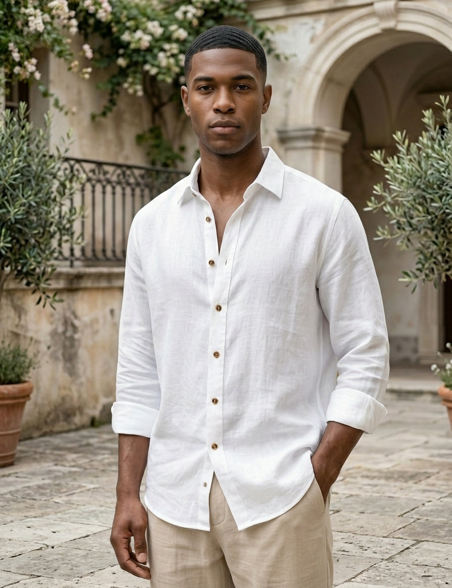 Man wearing a white button-up shirt and beige pants standing in an outdoor setting with architectural elements and plants.