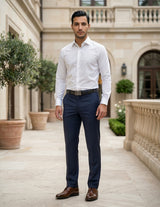 Man wearing a white dress shirt and navy pants standing in an elegant outdoor setting.