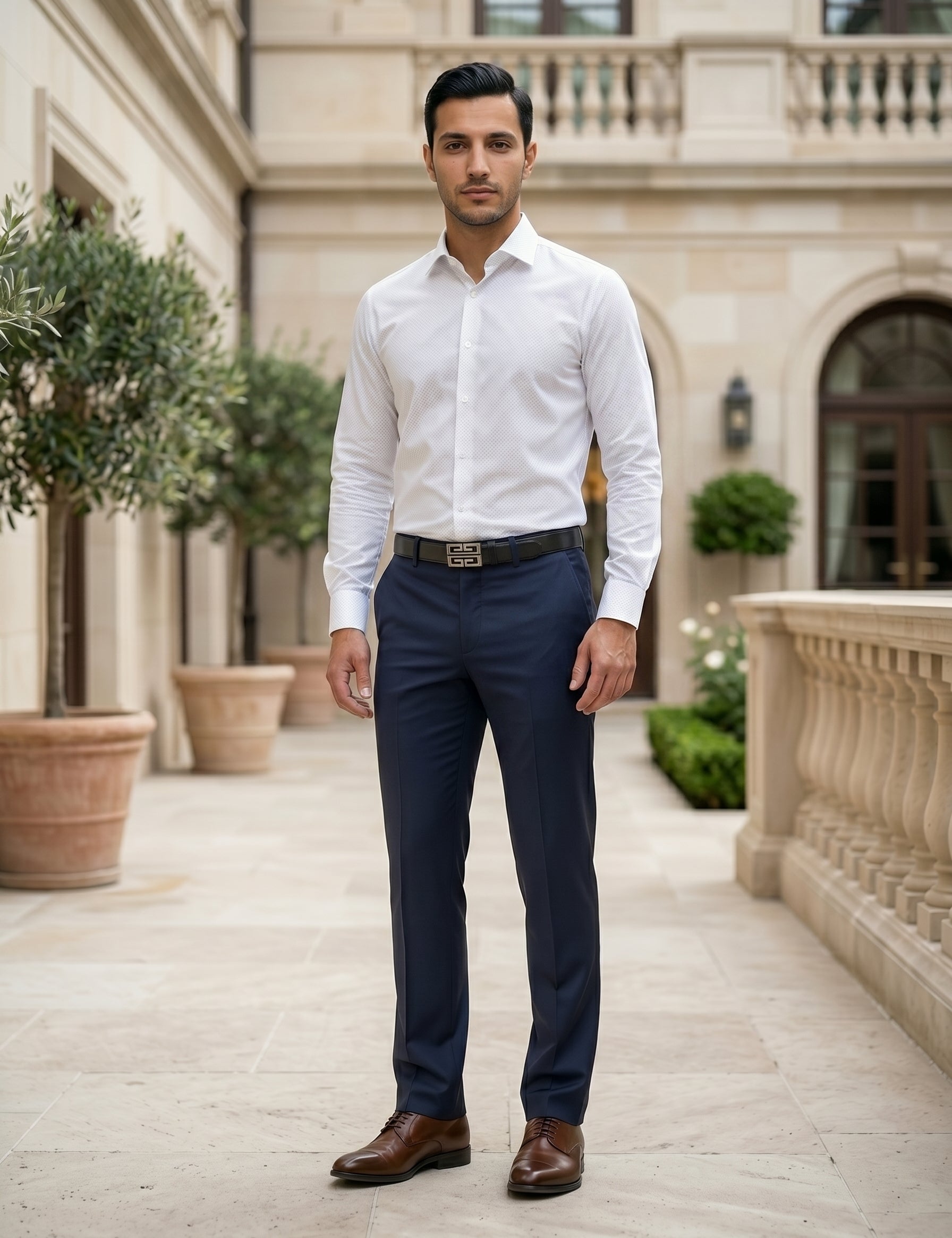 Man wearing a white dress shirt and navy pants standing in an elegant outdoor setting.