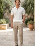 Man wearing a white polo shirt and beige pants standing outdoors with plants in the background