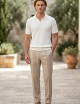 Man wearing a white polo shirt and beige pants standing outdoors with plants in the background