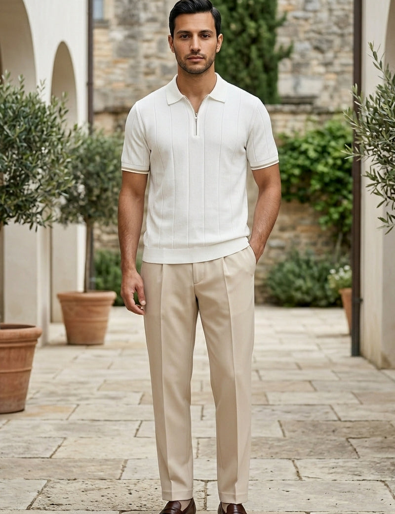 Man wearing a white polo shirt and beige pants standing in an outdoor setting with potted plants.