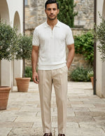 Man wearing a white polo shirt and beige pants standing in an outdoor setting with potted plants.