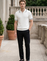 Man wearing a white polo shirt with black trim and black pants standing outdoors.