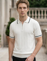 Man wearing a white polo shirt with black trim standing outdoors.