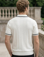 Man wearing a white polo shirt with black trim standing outdoors.