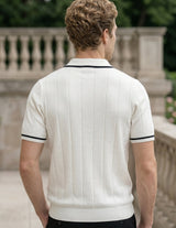 Man wearing a white polo shirt with black trim standing outdoors.