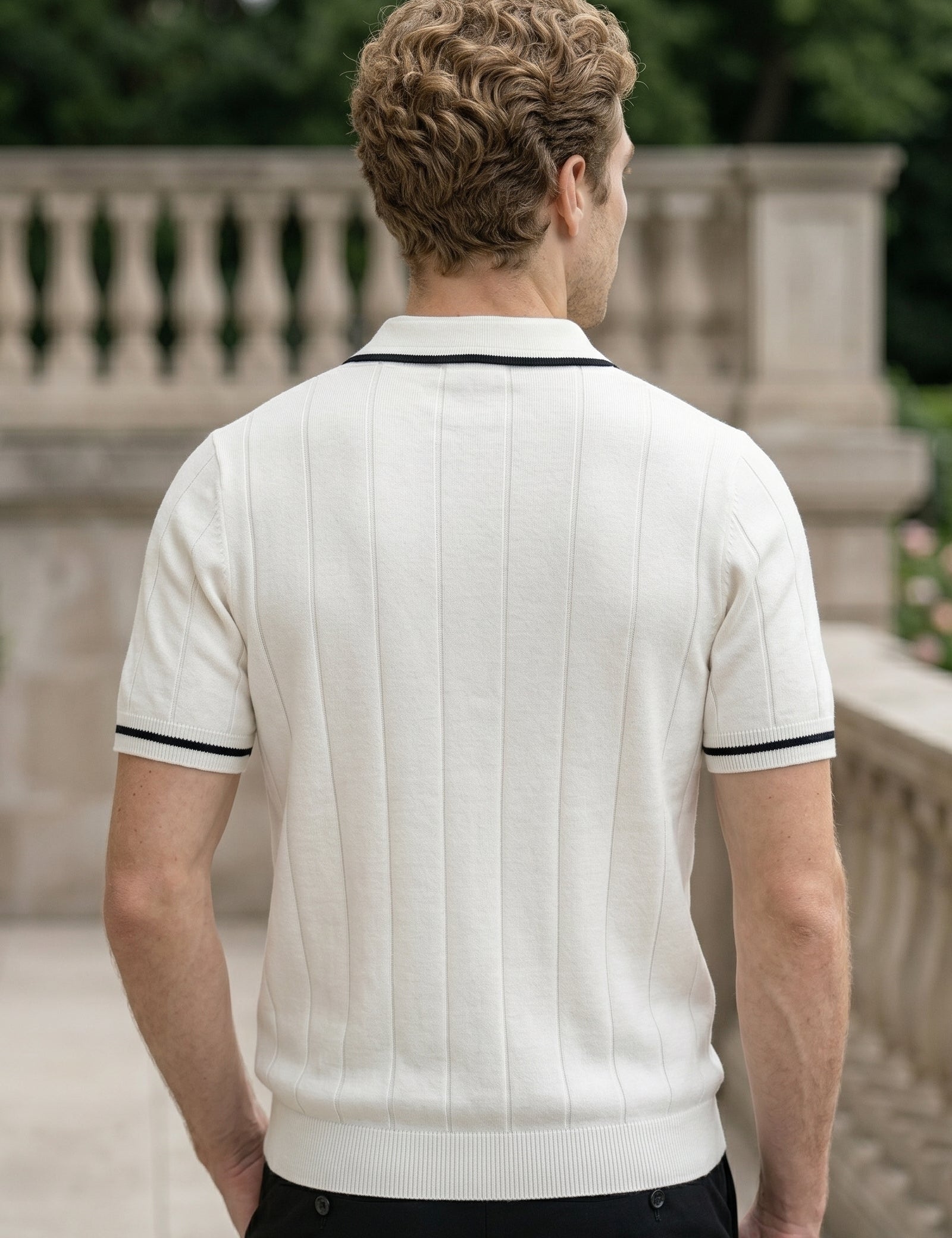 Man wearing a white polo shirt with black trim standing outdoors.