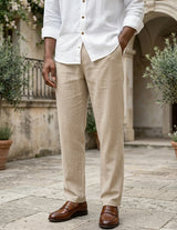 Man wearing a white shirt and beige pants with brown shoes in an outdoor setting.
