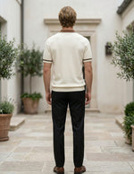Man wearing a white shirt and black pants standing in an outdoor setting with plants.
